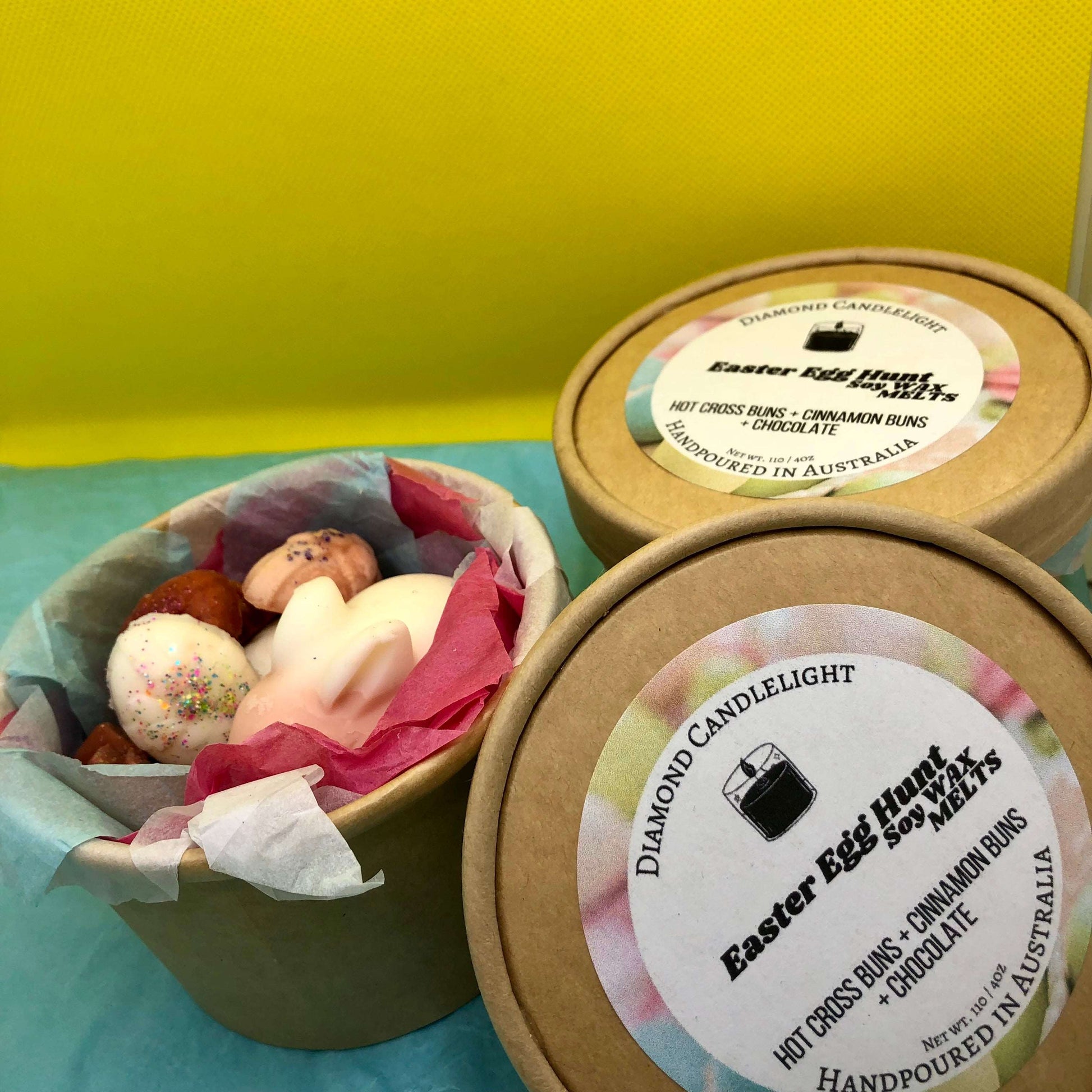 A tub of Easter Egg Hunt 110g Wax Melts with multiple colors visible, placed on a surface with a yellow background.